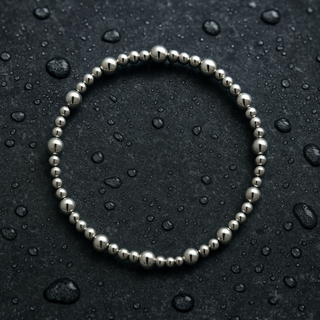 Silver beaded bracelet on a dark surface with water droplets
