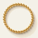 A gold beaded bracelet with polished spherical beads, arranged in a circular shape on a light cream background.