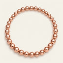 A stretch bracelet made of polished metallic rose gold beads, arranged in a circular shape on a light cream background.