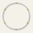 A delicate beaded necklace featuring a primary strand of small silver-toned beads and five spaced gold-toned accent beads, displayed on a light cream background.