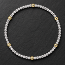 A beaded stretch bracelet featuring a mix of polished silver and yellow gold beads, arranged in a circular shape on a dark textured slate background.