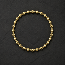 A gold beaded bracelet arranged in a circle on a dark textured slate background.