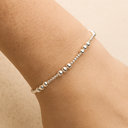 Silver beaded anklet on a person's wrist against a beige background