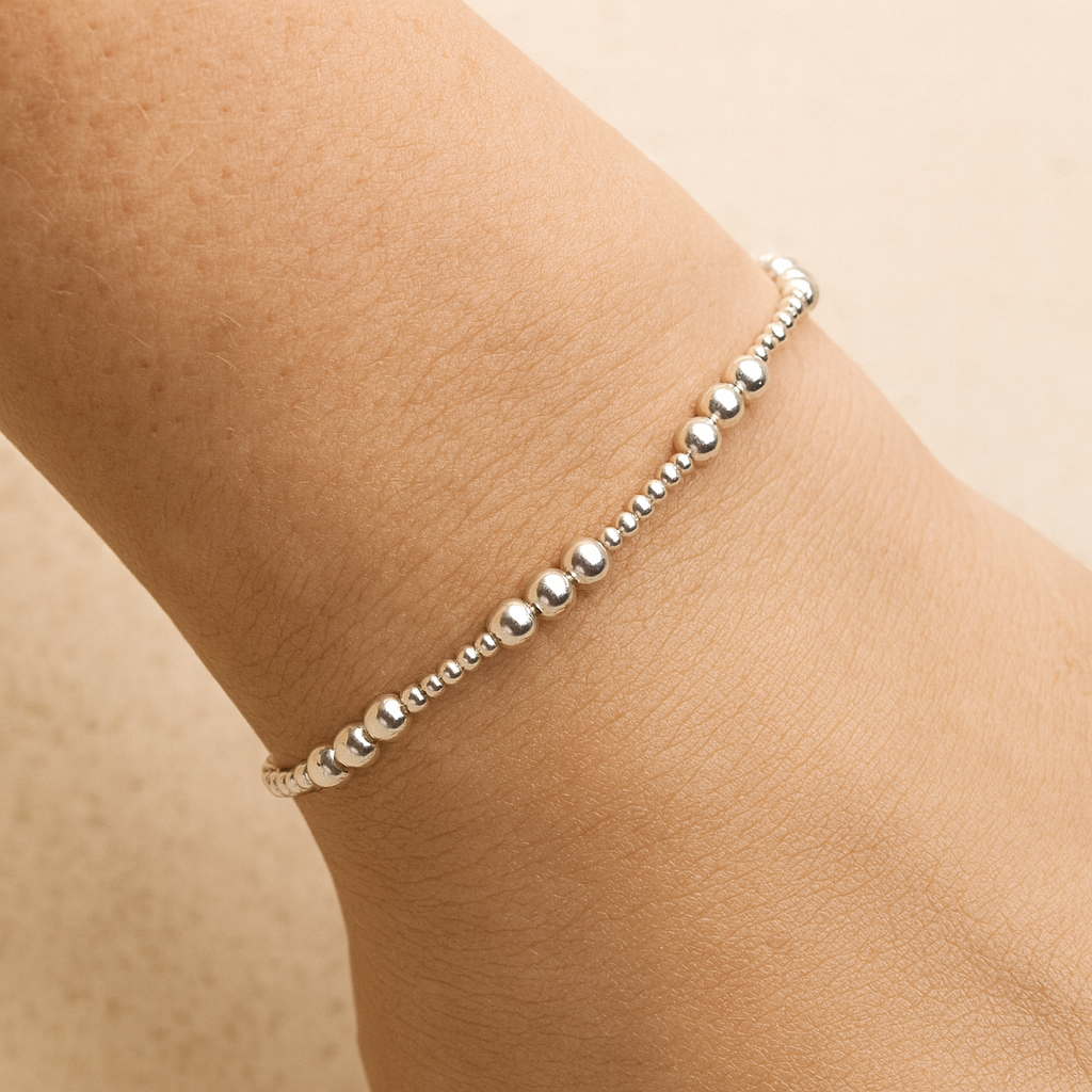 Silver beaded anklet on a person's wrist against a beige background
