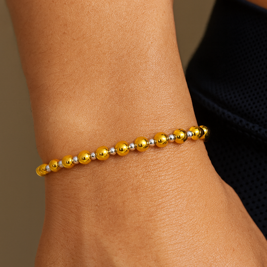 Gold beaded bracelet on a wrist with a neutral background