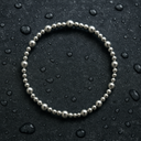 Silver beaded bracelet on a dark surface with water droplets